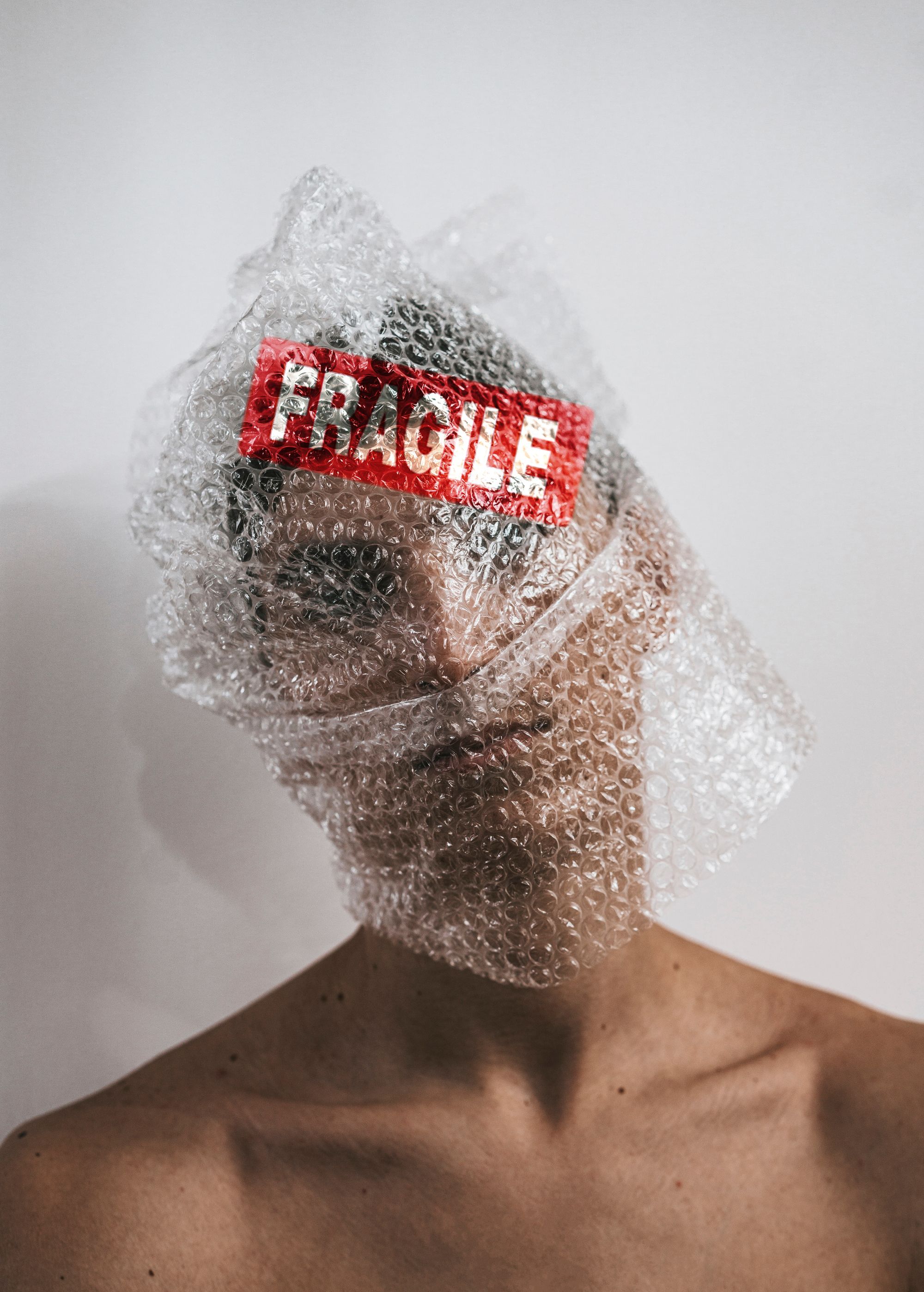 A person with bubble wrap around their head and a red sticker with the word fragile in white text